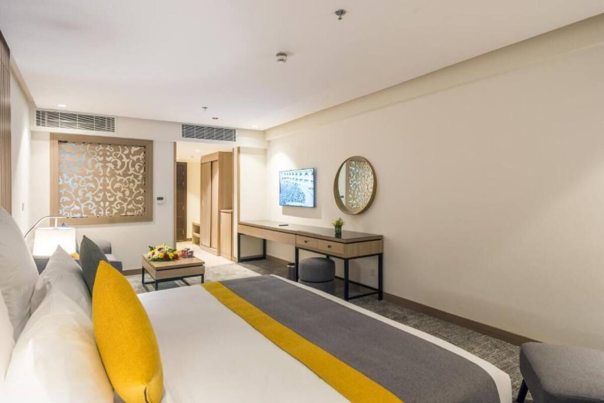 A modern hotel room with a large bed, a desk, a television, and a decorative wall piece.