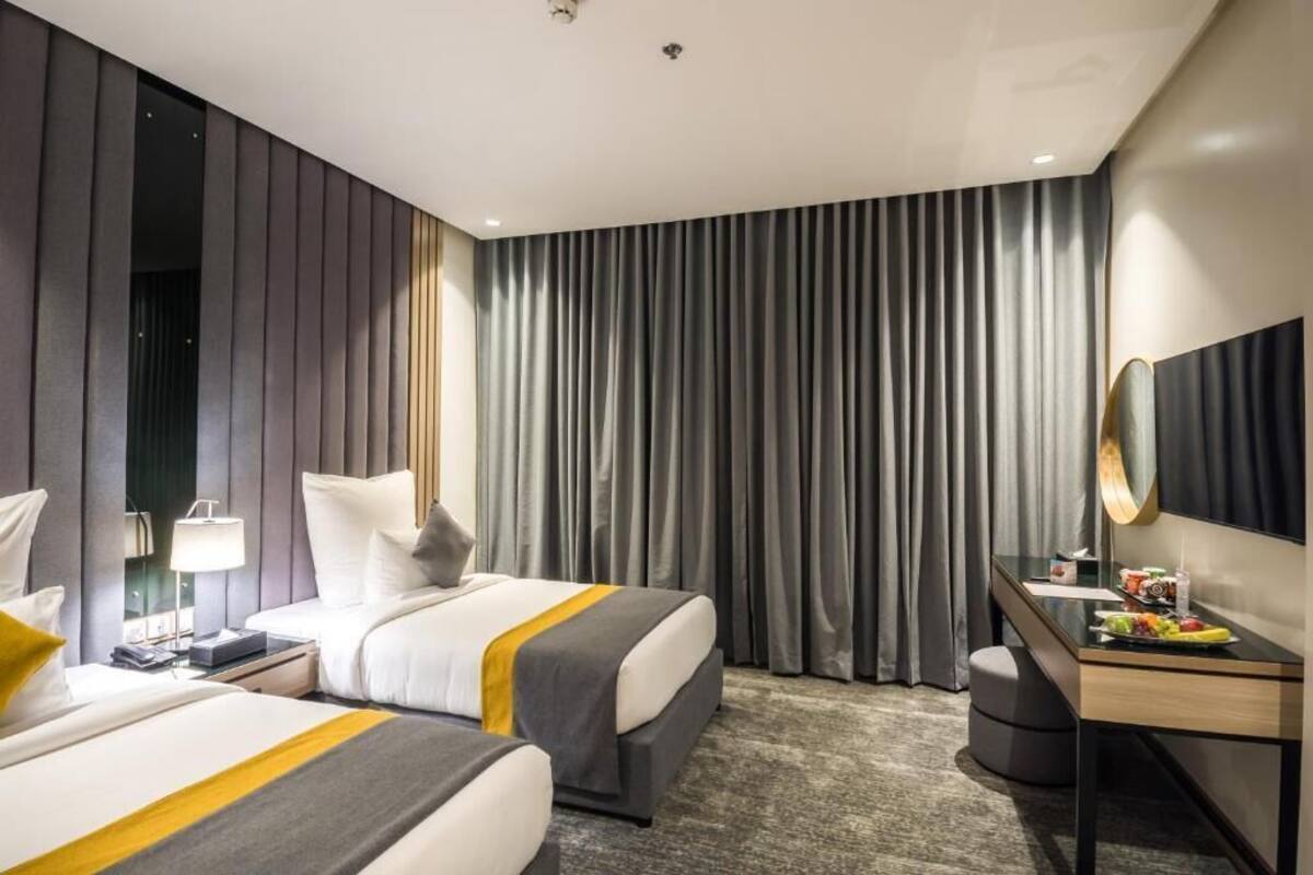 A hotel room with two beds, a desk, a chair, a mirror, and a large window with curtains.