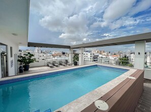 A rooftop pool with a city view, lounge chairs, and potted plants.