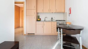Une cuisine compacte avec des meubles de couleur bois clair, une cuisinière à gaz et une petite table à manger.
