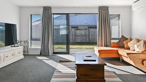 Un salon moderne avec un canapé, un téléviseur et une grande porte-fenêtre coulissante donnant sur un jardin.