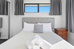 A neatly made bed with a tufted headboard, two pillows, and a folded towel on the bed.