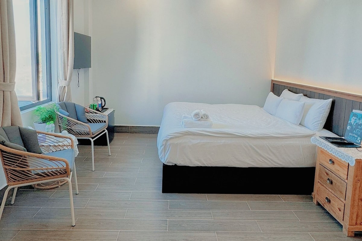 Una habitación de hotel moderna con una cama grande, un televisor de pantalla plana, una mesita de noche y una zona de estar con sillas.