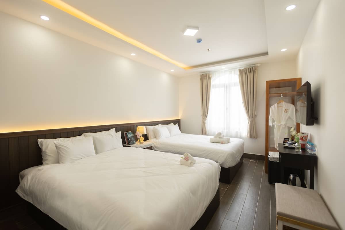 Habitación de hotel con dos camas, una mesita de noche con lámpara, un espejo y un televisor montado en la pared.