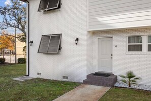 Un bâtiment en briques blanches, avec une porte blanche, une petite fenêtre et un escalier menant à l’entrée.