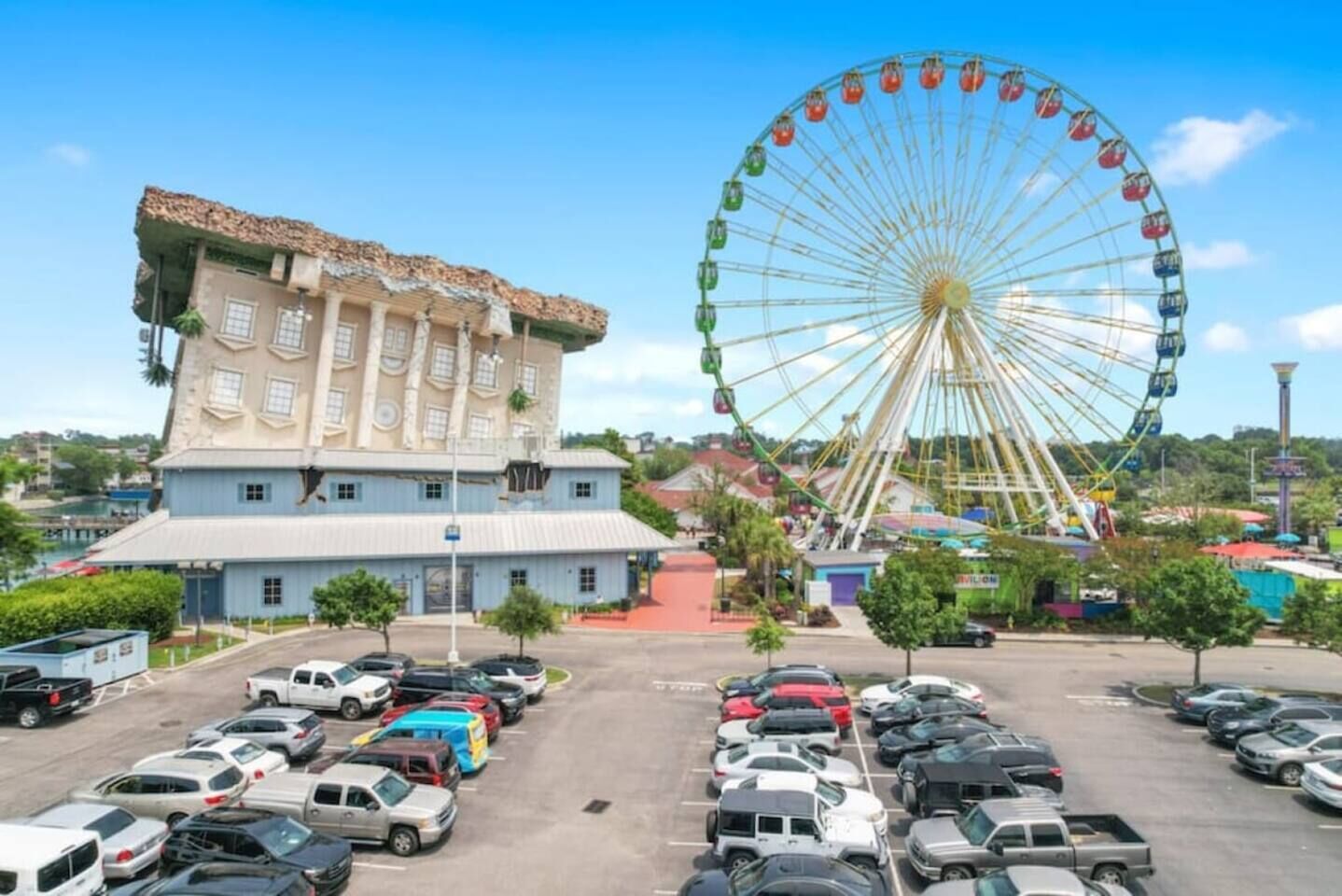 A parking lot with multiple cars, a large Ferris wheel, and a building with a unique architectural style.