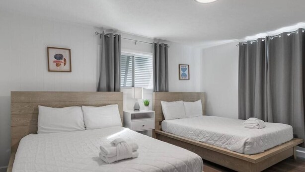 A hotel room with two beds, a bedside table, a lamp, and a window with curtains.