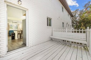 A white wooden house with a deck, a white fence, and a door leading to an interior space with a blue chair and a trash bin. - Azul Condos 4 | 2 Bedroom, Near Ocean, Kitchen (Myrtle Beach)
