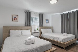 Une chambre d’hôtel avec deux lits simples, une petite table de chevet avec une lampe et une fenêtre avec des rideaux.