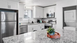 A modern kitchen with stainless steel appliances, white cabinetry, and a granite countertop.
