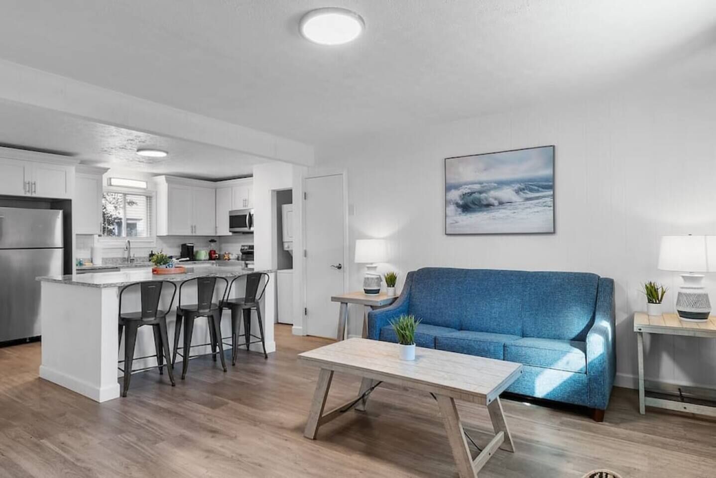A modern kitchen with white cabinets, a central island with bar stools, a blue sofa, and a wooden coffee table.