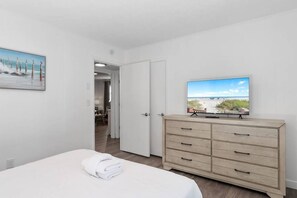 Ein Hotelzimmer mit einem Bett, einem Fernseher auf einer Kommode, einem Bild an der Wand und einer Tür zu einem anderen Raum.