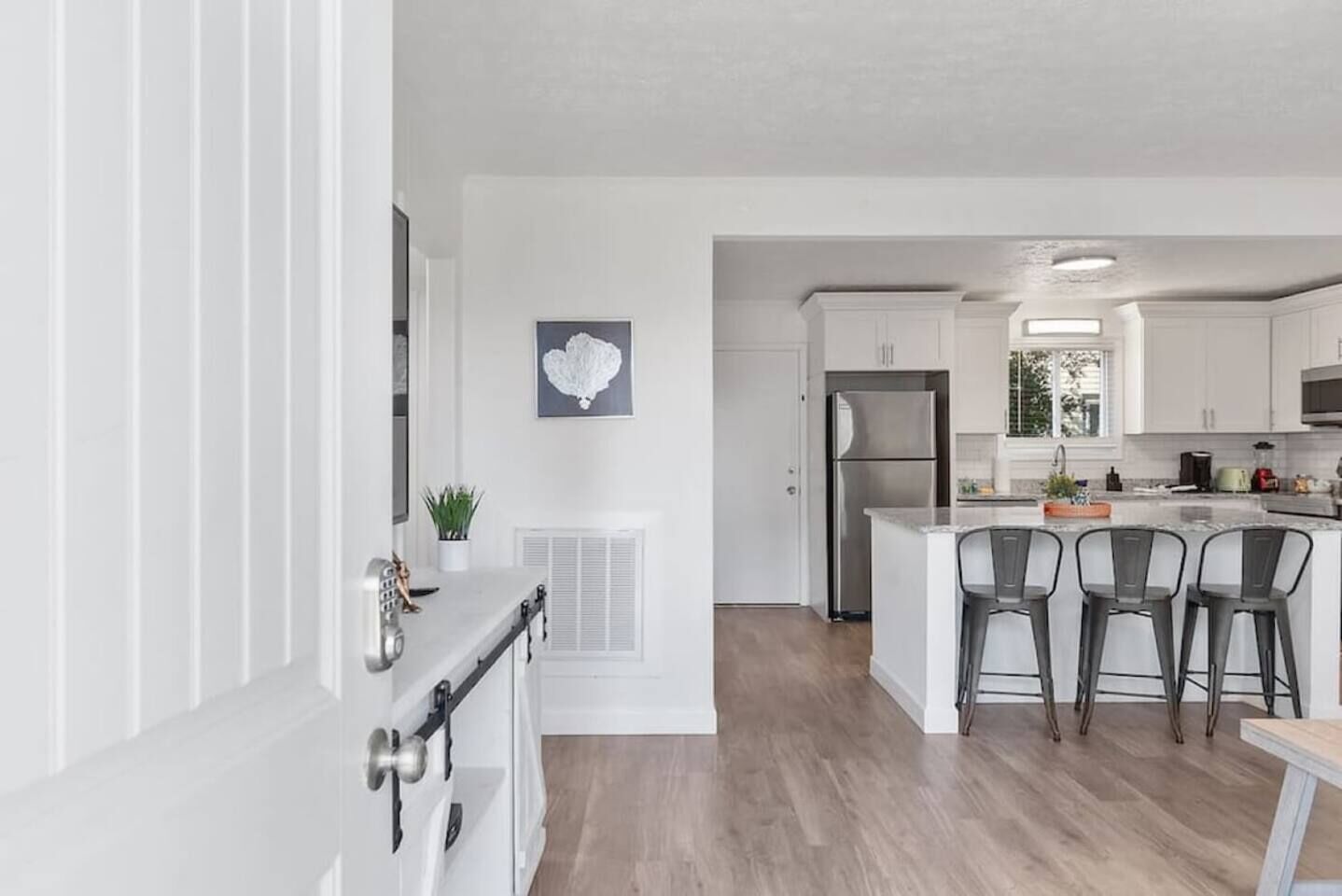 A modern kitchen with a central island, bar stools, and a stainless steel refrigerator.