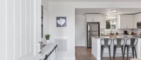 Una cocina moderna con una isla central, taburetes de bar y un refrigerador de acero inoxidable.