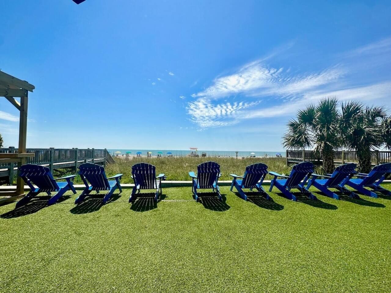 A beachside lounge area with rows of blue lounge chairs and a wooden pergola.