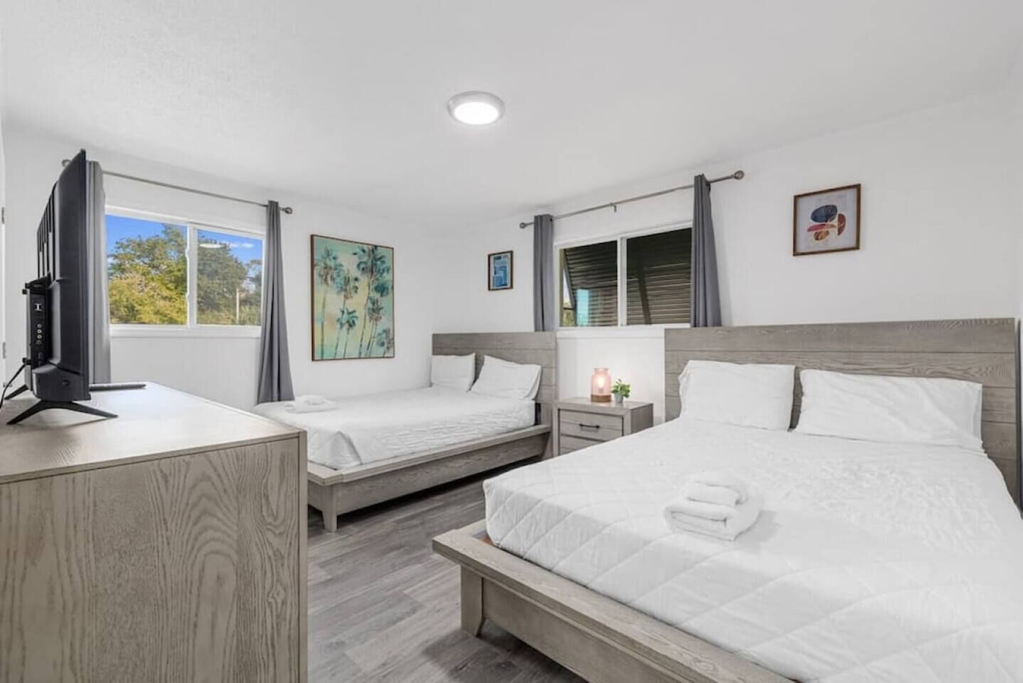A hotel room with two beds, a desk, a television, and artwork on the walls.