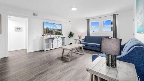 Ein modernes Wohnzimmer mit einer Couch, einem Couchtisch und einem Fernseher. Ein Fenster bietet Blick auf den Himmel.