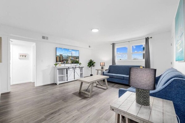 A modern living room with a sofa, a coffee table, and a TV. There is a window with a view of the sky.