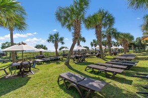 An outdoor seating area with tables and chairs, surrounded by palm trees and umbrellas.