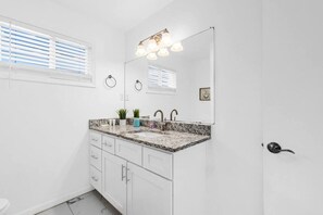 A bathroom with a white vanity, a sink, a mirror, and a door.