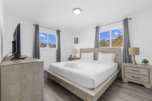 A hotel room with a bed, bedside tables, a TV, and windows with curtains.