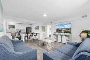 A modern living room with a dining area, kitchen, and a large TV displaying a cityscape.