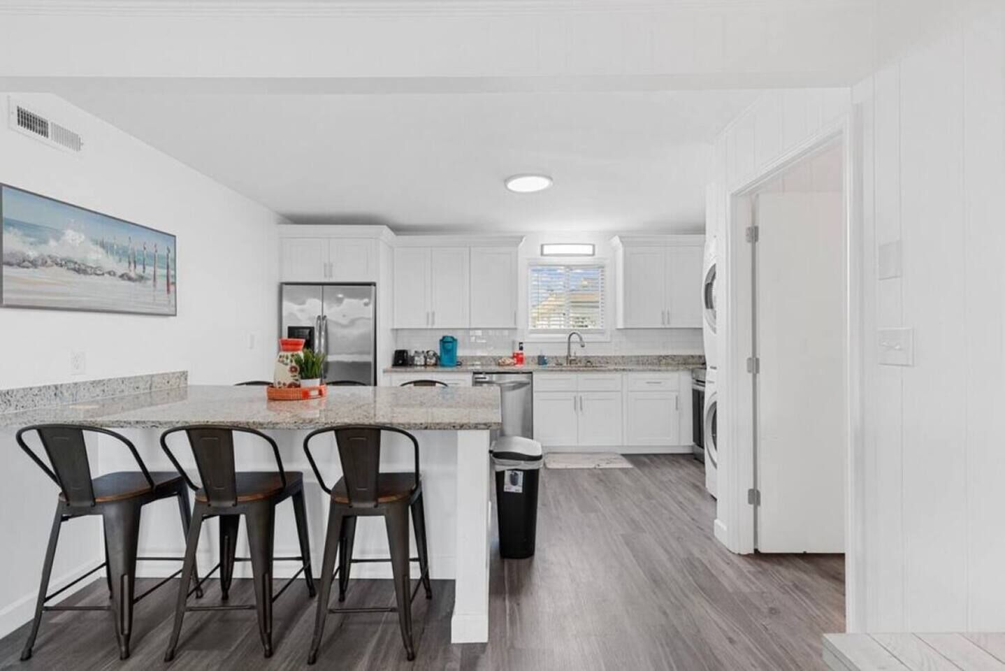 Een moderne keuken met witte kasten, een granieten aanrechtblad en een inbouw eiland met barstoelen.