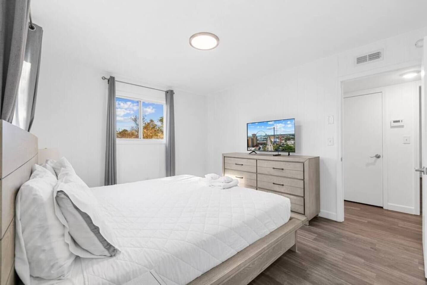 Une chambre à coucher avec un lit, une commode, un téléviseur et une fenêtre avec des rideaux.