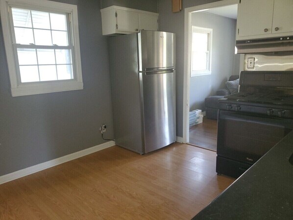 Una cocina con un refrigerador de acero inoxidable, una estufa negra y piso de madera.