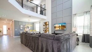 Een ruime woonkamer met een grote hoekbank, een hoge plafond en een balkon.