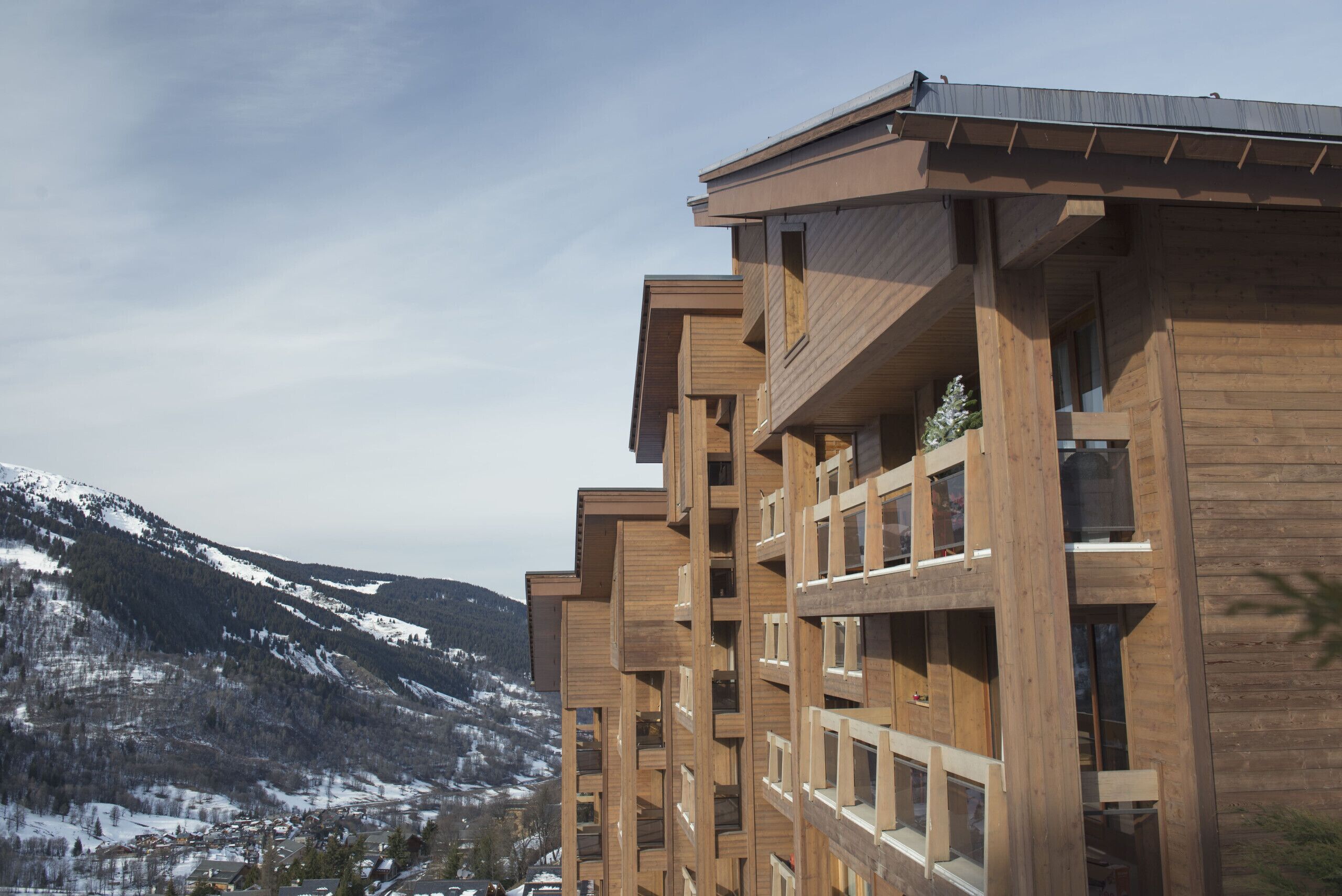 A multi-story wooden building with balconies, set against a snowy mountain backdrop.