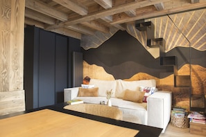 A modern interior with a wooden ceiling, a white sofa with cushions, a wooden table, and a wall with a mountain-like design.