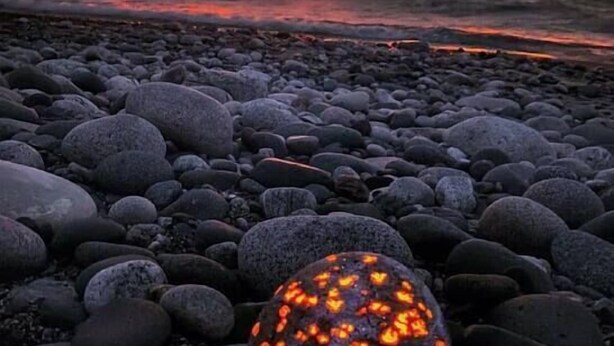 Una playa con atardecer, piedras y un objeto brillante.