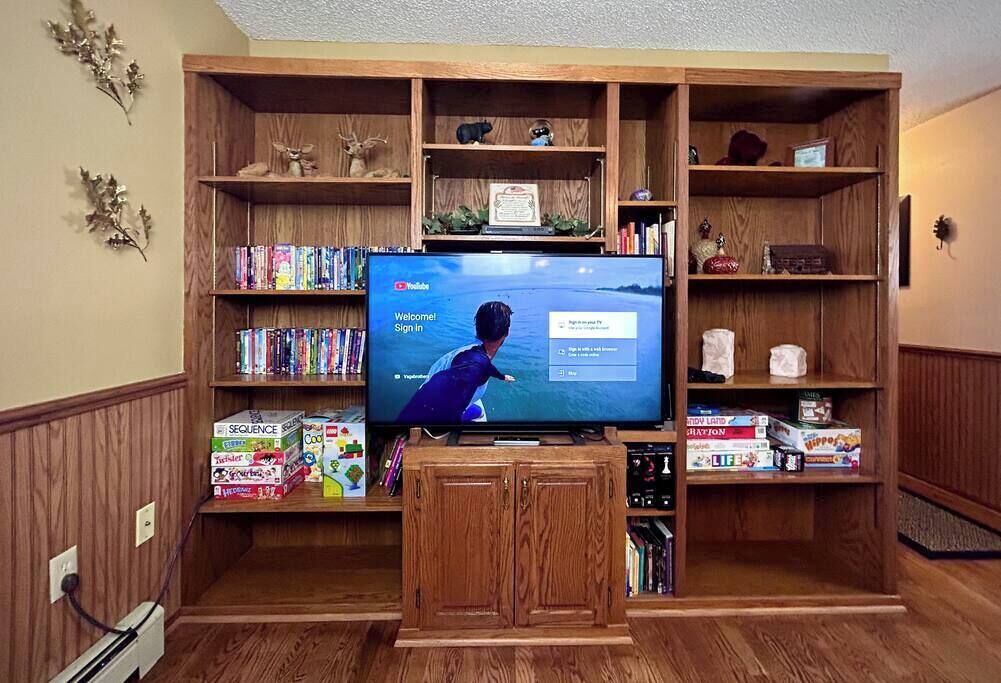 Ein Wohnzimmer mit Flachbildfernseher auf einem Holzboden, umgeben von Regalen mit Büchern und Dekorationsobjekten.