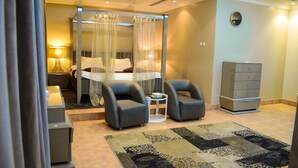 A bedroom with a canopy bed, two armchairs, a nightstand, a dresser, and a rug. - ARJAN QURTUBA SERVICED APARTMENTS (Al Khobar)