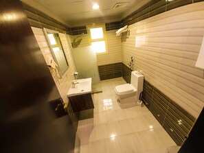 A modern bathroom with a toilet, sink, and mirror. - ARJAN QURTUBA SERVICED APARTMENTS (Al Khobar)