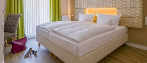 A hotel room with two beds, a grey armchair, a pink bag, and a wooden floor.