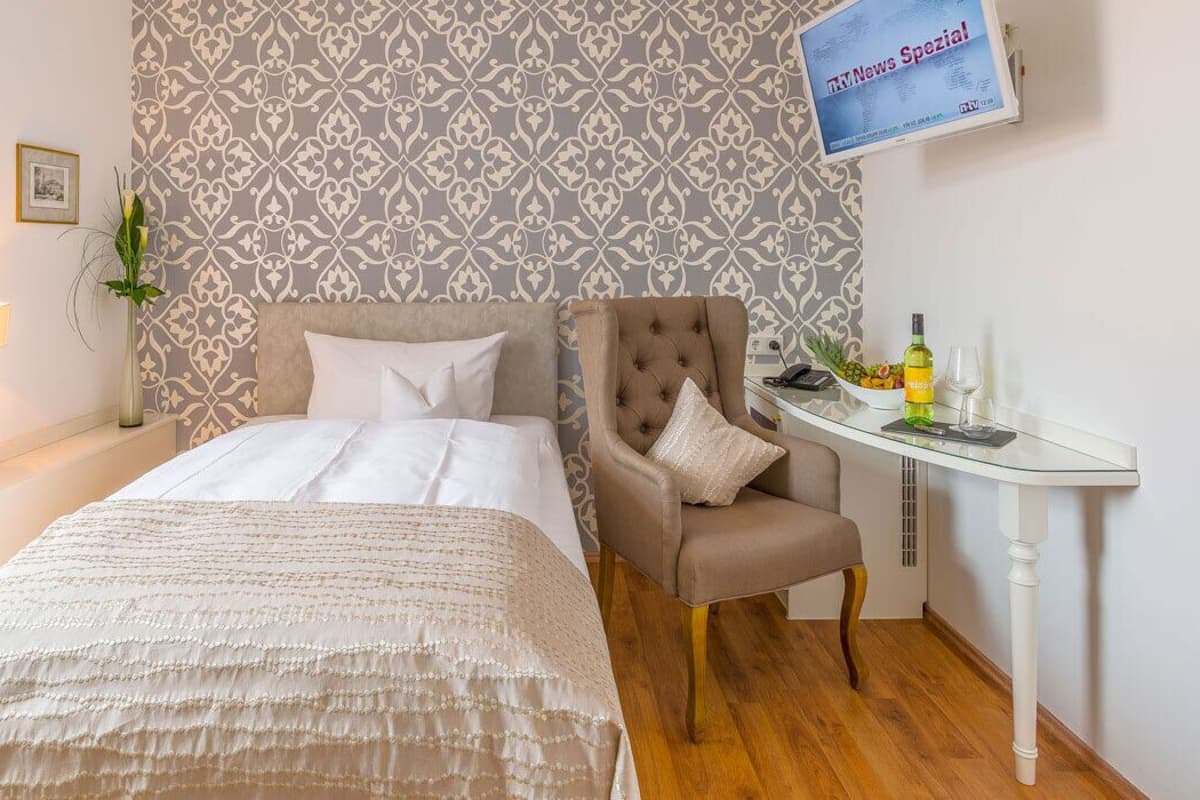 A hotel room with a bed, a chair, a small table with a bottle and glass, and a TV displaying 'TV News Special'.
