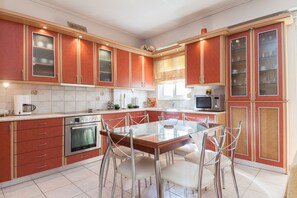A modern kitchen with red cabinets, stainless steel appliances, and a glass dining table.