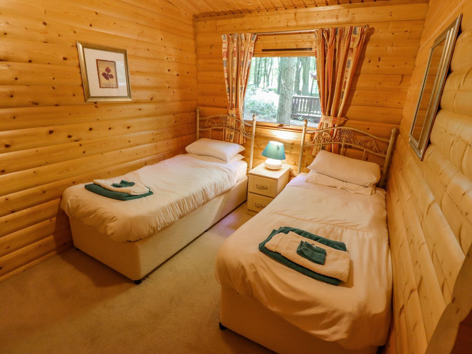 A cozy wooden cabin room with two single beds, a nightstand with a lamp, and a window with curtains.
