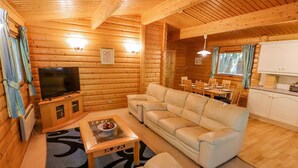 A log cabin interior with a living room, sofa, TV, dining area, and kitchen. - Bamboo Retreat (Louth)