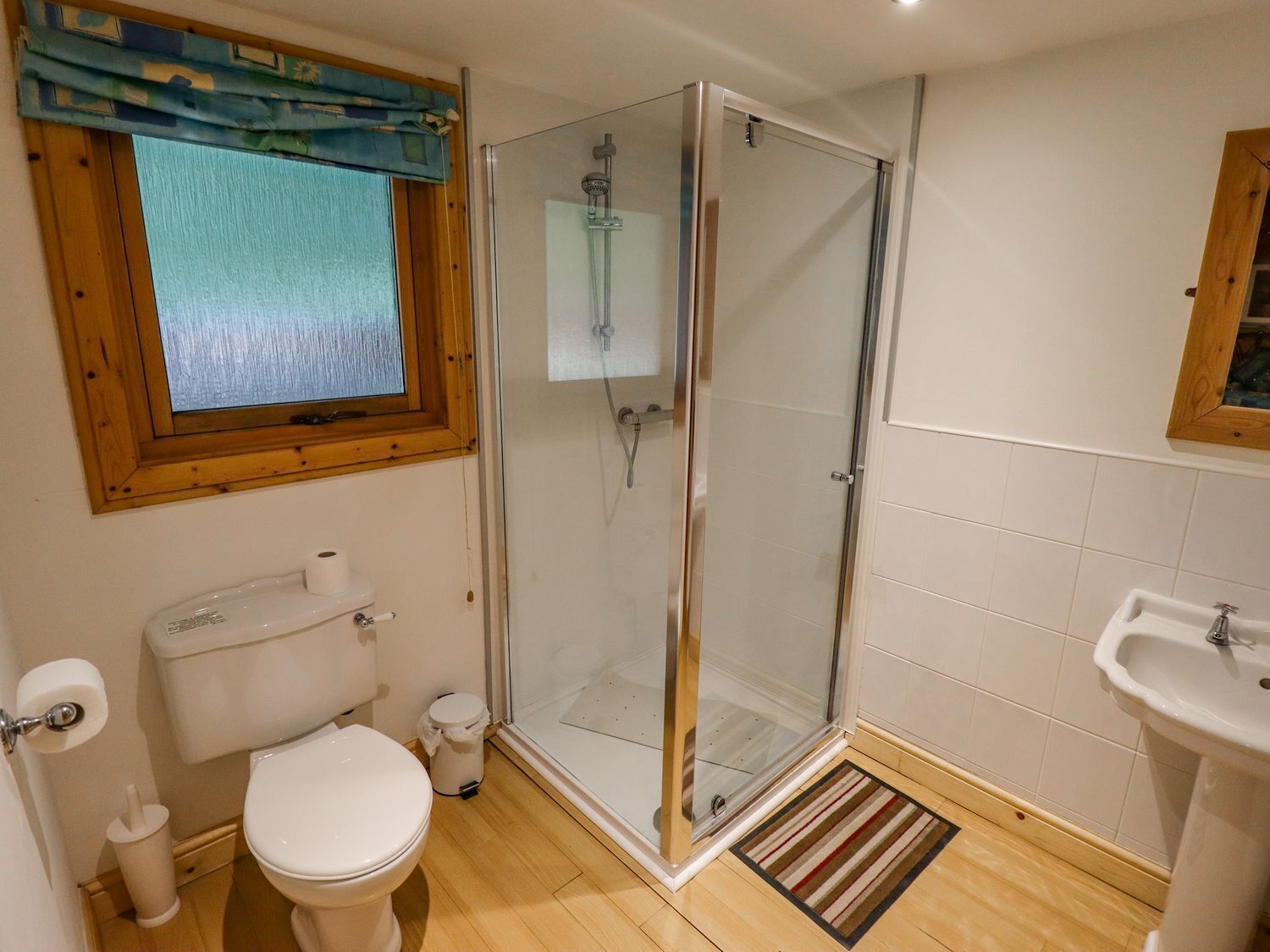 A bathroom with a glass shower enclosure, toilet, sink, and a window with a view.