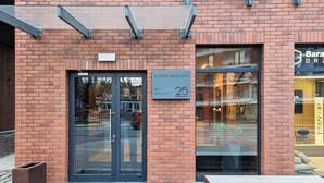 A brick building with a glass door entrance, a bench outside, and a sign indicating the address as 25. - Modern Studio in the Center | Balcony and Workspace (Gdańsk)