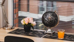 A desk with a globe, a lamp, a vase with flowers, and a glass of orange juice. - Modern Studio in the Center | Balcony and Workspace (Gdańsk)
