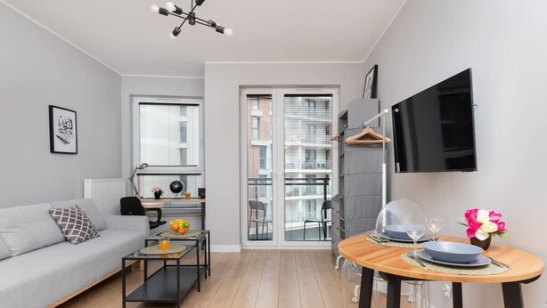 A modern living room with a sofa, coffee table, and a dining area with a table and chairs. - Modern Studio in the Center | Balcony and Workspace (Gdańsk)