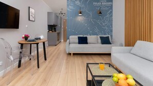 A modern living room with a grey sofa, a dining table with chairs, a kitchen area, and a wall map. - Modern Studio in the Center | Balcony and Workspace (Gdańsk)