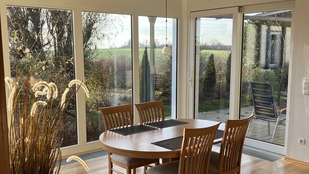 Un comedor amplio con una mesa redonda y seis sillas, ventanas grandes que ofrecen vistas al exterior y un techo con lámparas colgantes.