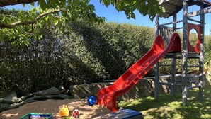 Un parque infantil con un tobogán rojo, zona de juegos con arena y una estructura para escalar.