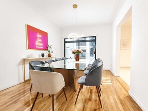 Un espace repas moderne avec une table en verre, des chaises grises et un néon mural.