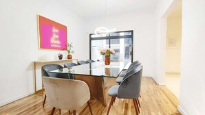 A modern dining area with a glass table, grey upholstered chairs, and a wooden floor.